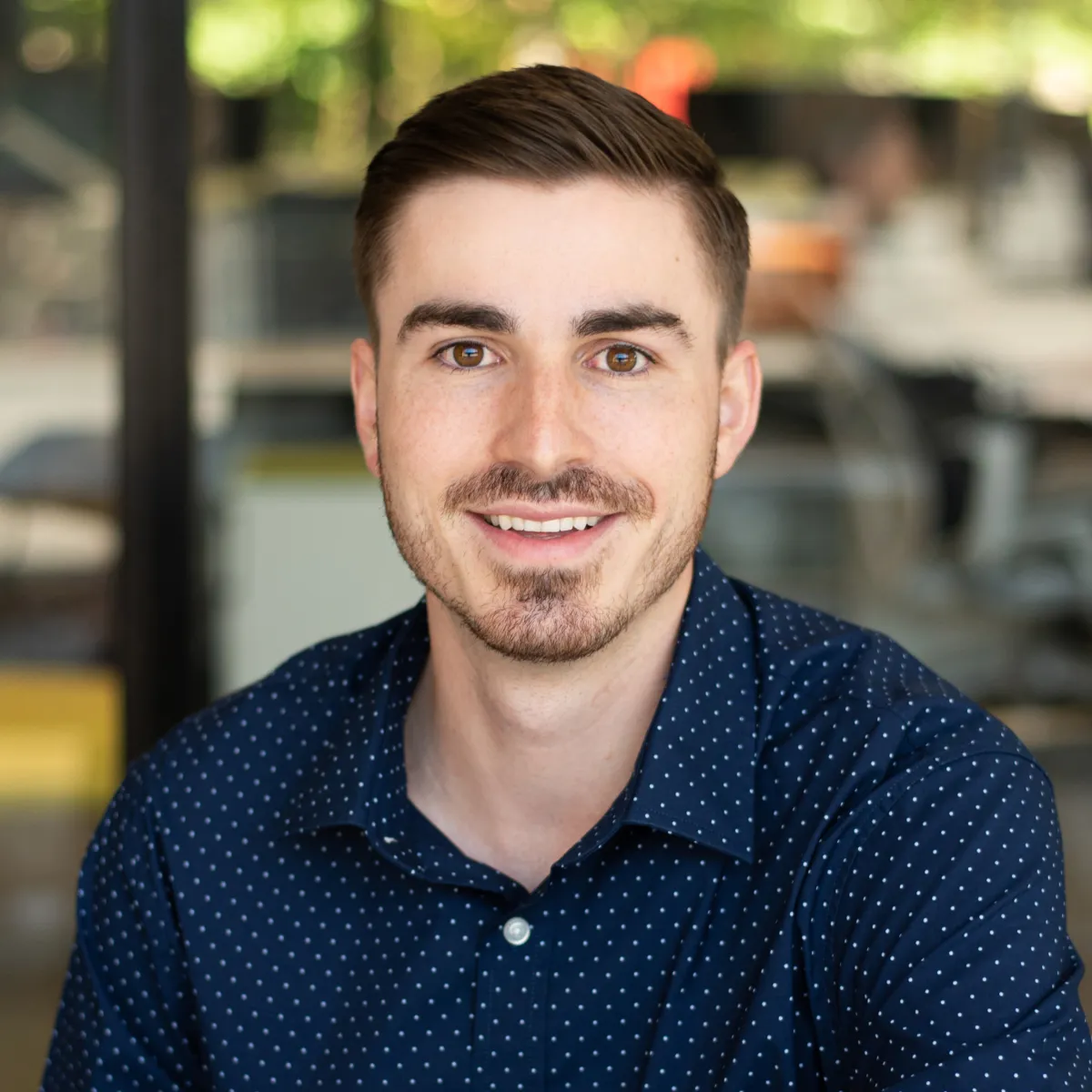 Alex Keiser smiling, wearing a navy polka dot button down shirt
