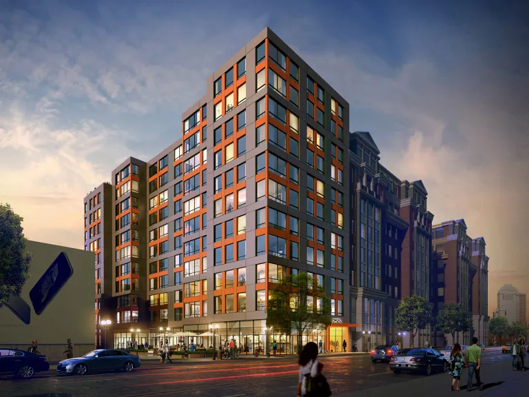 Exterior view of a multi-family housing unit on a busy street in the evening.