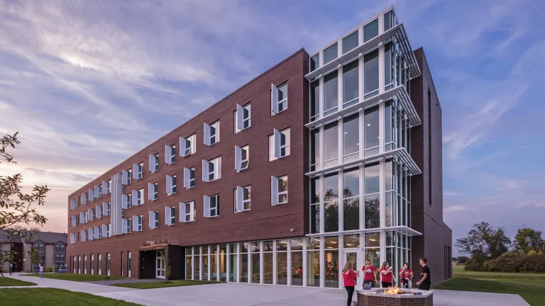 Exterior of McConnell Hall at dusk with five students interacting around a lit fire pit, wearing Ohio State gear