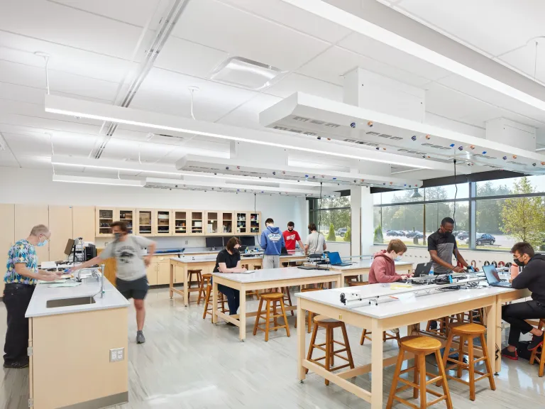 Alford physics lab featuring large group tables that are white and light wood and students interacting