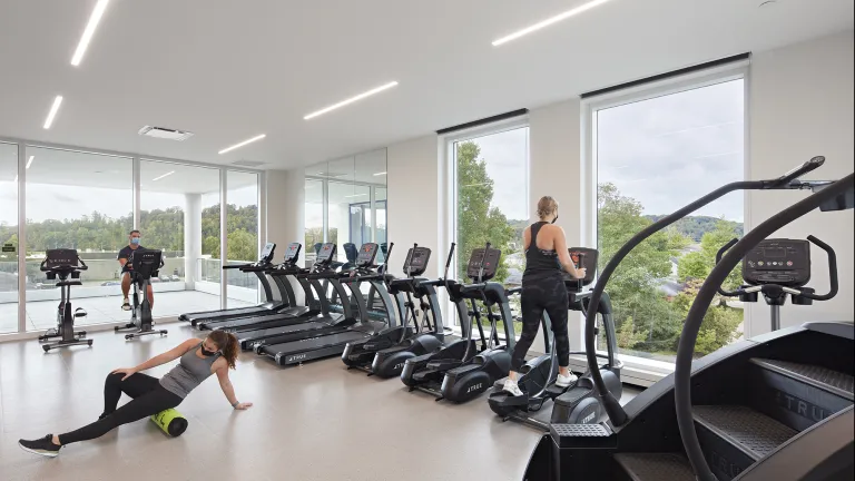 A group of people in a workout room on various workout machines and stretching.