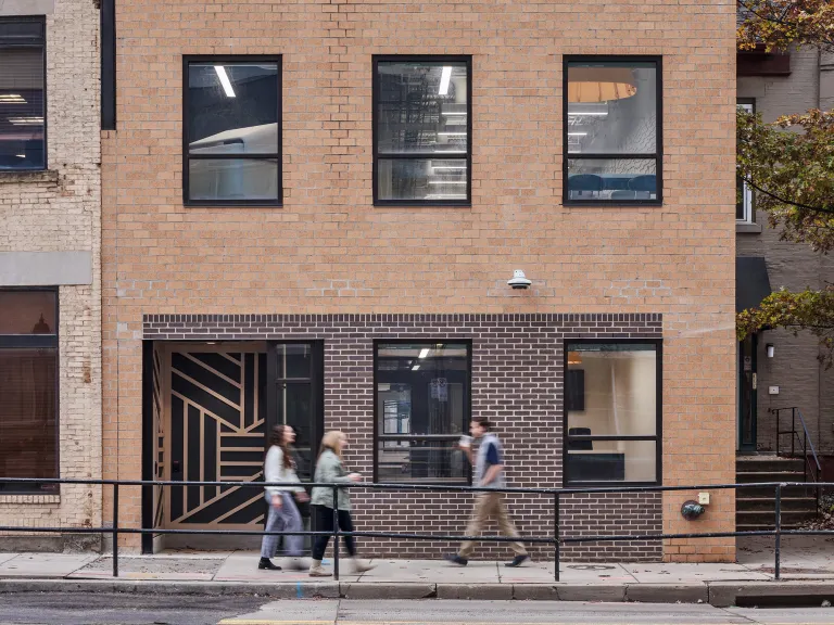 People walking past a brick building.