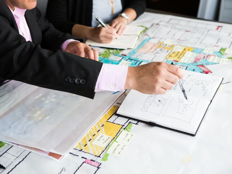 Two designers at a table with architectural plans and notes.